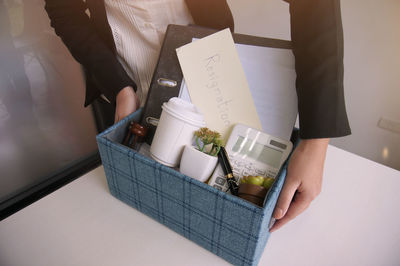 Midsection of woman holding office supply in crate on desk at office