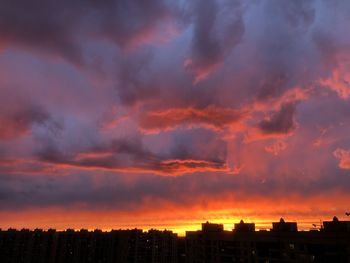 Silhouette buildings against dramatic sky during sunset