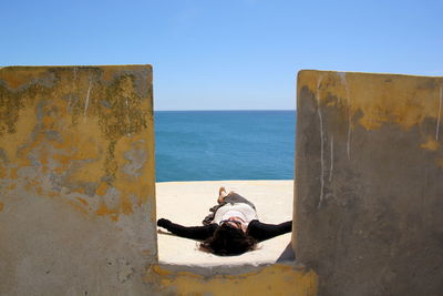 Woman relaxing on pier by sea against clear sky