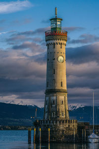 Lighthouse by building against sky during sunset