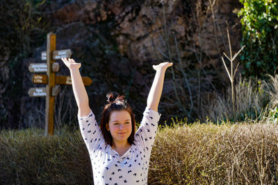 Smiling young woman with arms raised standing on field