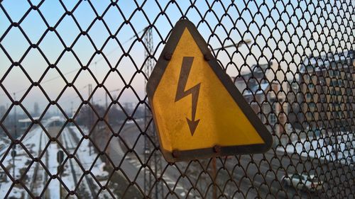 Close-up of yellow high voltage sign on chainlink fence