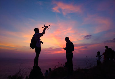 Silhouette couple with drone at beach during sunset