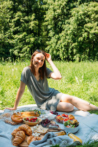 Portrait of young woman using mobile phone while sitting on field