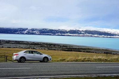 Car on road by sea against sky