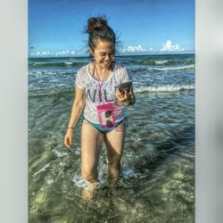 Full length of young woman playing in water at beach