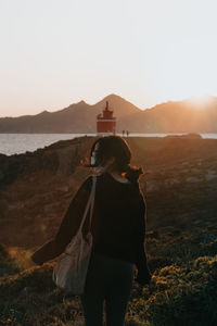 Rear view of woman standing on mountain against sky during sunset