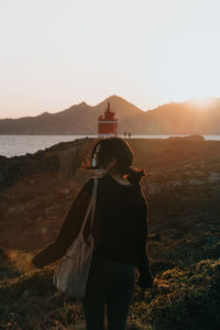 Rear view of woman standing at shore during sunset