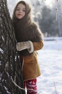 Portrait of smiling young woman standing by tree during winter