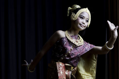 Cute girl wearing traditional clothing dancing against black background