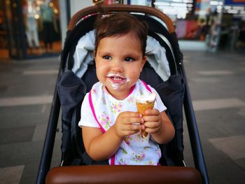 Cute girl eating ice cream while sitting in baby carriage