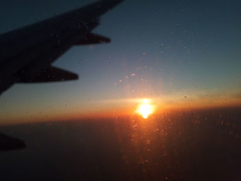 Close-up of wet airplane window against sky during sunset