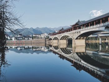 Arch bridge over river amidst buildings against sky