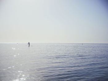 Mid distance view of silhouette man paddleboarding on sea against clear sky