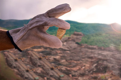 Close-up of human hand holding land against sky