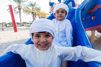 Portrait of smiling brothers wearing traditional clothing sliding in playground