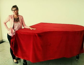 Happy woman standing by red fabric covering on piano against white wall