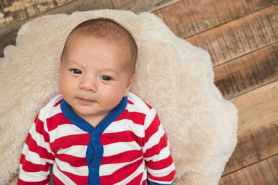 Directly above portrait of baby boy lying on rug over wooden floor