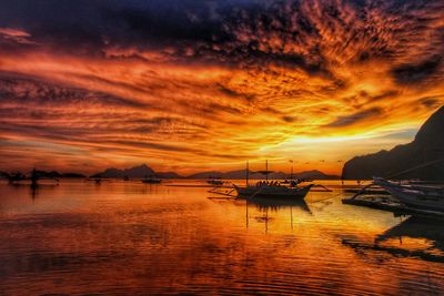 Outriggers moored in river against cloudy sky during sunset