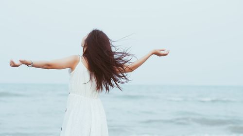 Rear view of woman standing with arms outstretched by sea against clear sky