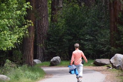 Rear view of woman walking on footpath along trees