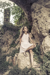 Girl looking away while sitting on rock in forest