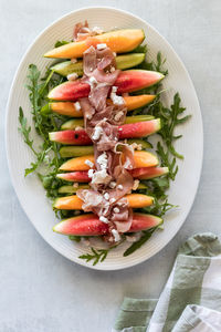 A platter of melon and cucumber wedges topped with prosciutto and feta.