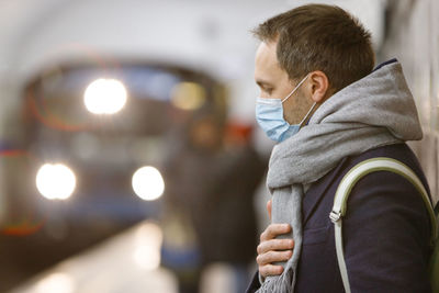 Exhausted man feeling sick, wearing protective mask against transmissible infectious diseases.