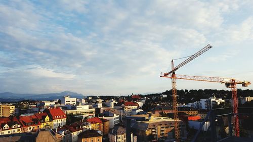 Cranes by buildings in city against sky