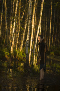 Side view of smiling woman standing in lake against trees at forest