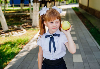 Back to school. a little schoolgirl stands in the school yard and holds an apple in her hands.