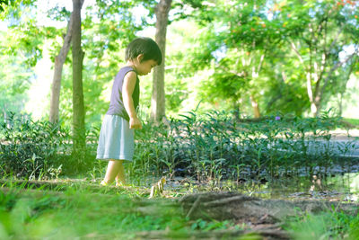 Side view of boy standing on grass against trees