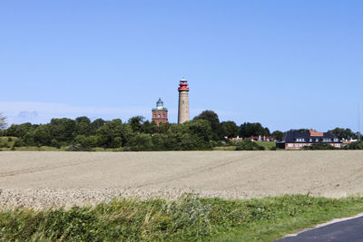 Lighthouse on field by building against clear blue sky