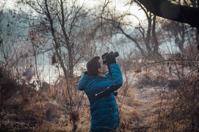 Man photographing by bare trees in forest