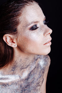 Close-up of young woman with silver bodypaint over black background