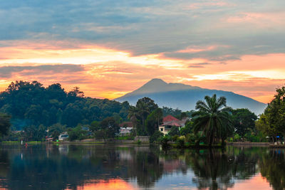Scenic view of lake by trees against orange sky