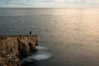 Man standing on rock by sea against sky