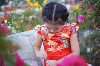 Girl holding flowers while sitting on bench by flowering plants