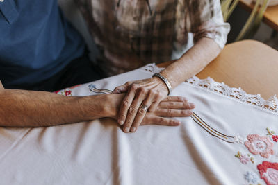 Senior woman holding hand of male caregiver over tablecloth at home