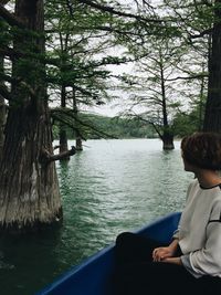 Rear view of man sitting on tree trunk by lake