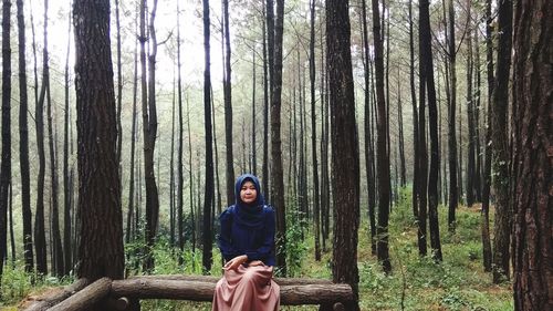 Young woman sitting on tree trunk in pine forest