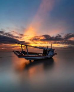 Boat moored on sea against sky during sunset