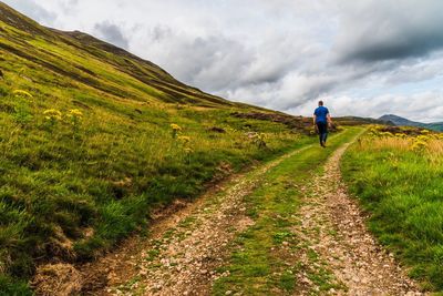 Rear view of man walking on field against sky