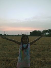 Girl standing on field against sky during sunset