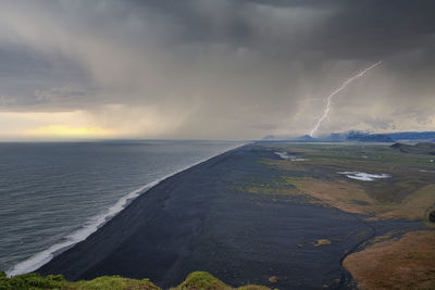 Lightning weather over black sand beach against cloudy sky during sunset