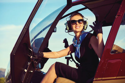 Portrait of smiling young woman sitting in car against sky