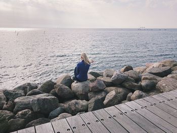 Rear view of woman sitting on rock against sea at beach