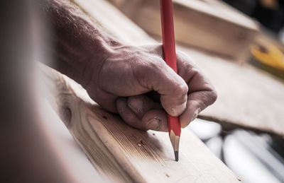 Cropped hand of man marking on wood at workshop