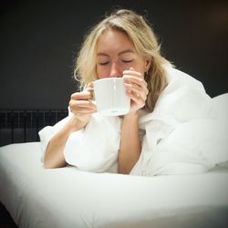 Close-up of young woman drinking coffee cup on bed at home