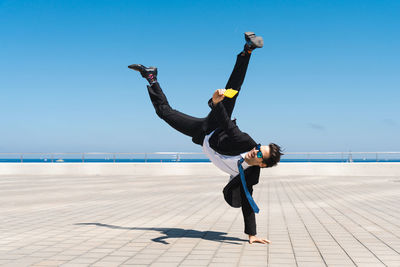 Full length of woman jumping on beach against clear blue sky